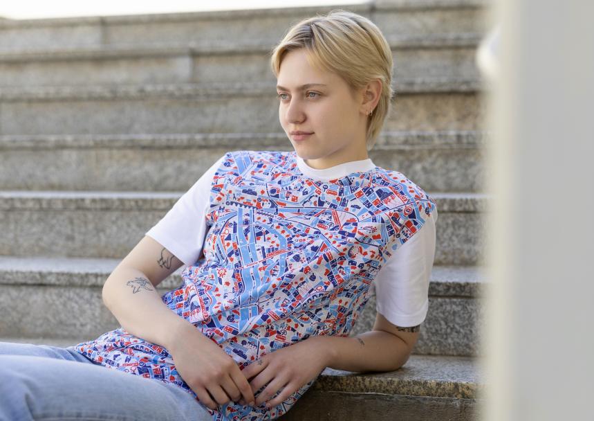 Junge Frau mit T-Shirt aus der Ganz Wien Sommerkollektion lehnt lässig auf Stufen im Freien