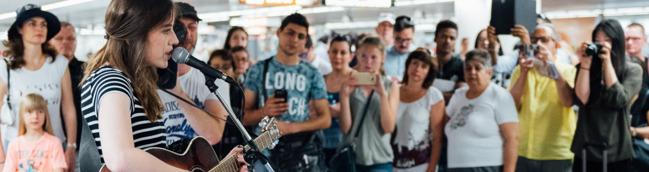 viele Menschen in der U-Bahn stehen rund um eine Sängerin mit Mikrophon