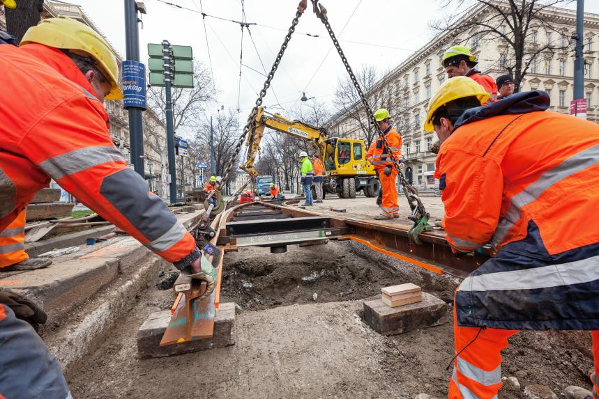 Construction workers lift new tram tracks into the track bed