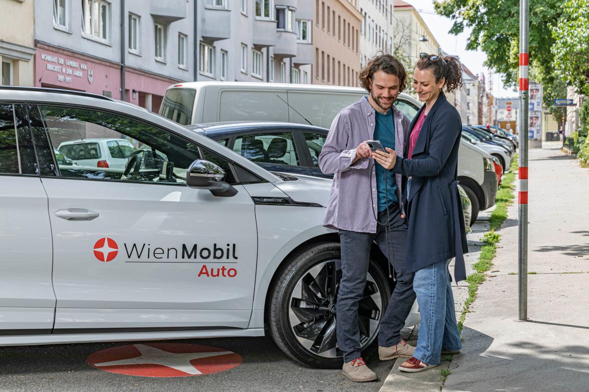 two people looking at a smartphone in front of a WienMobil car