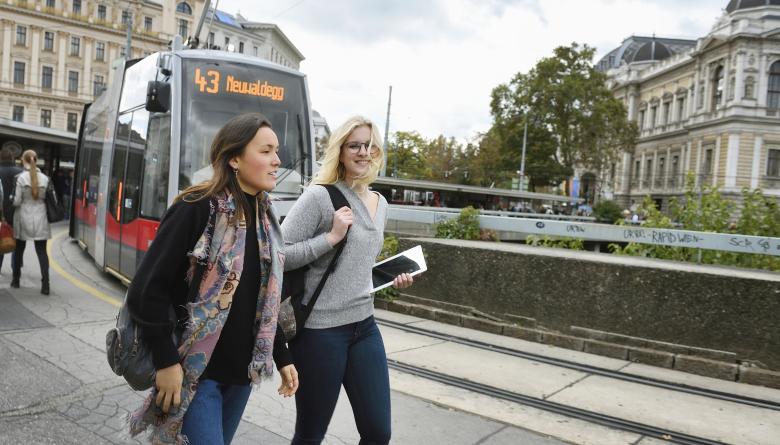 2 junge Frauen vor einer Straßenbahn im Hintergrund die Hauptuniversität