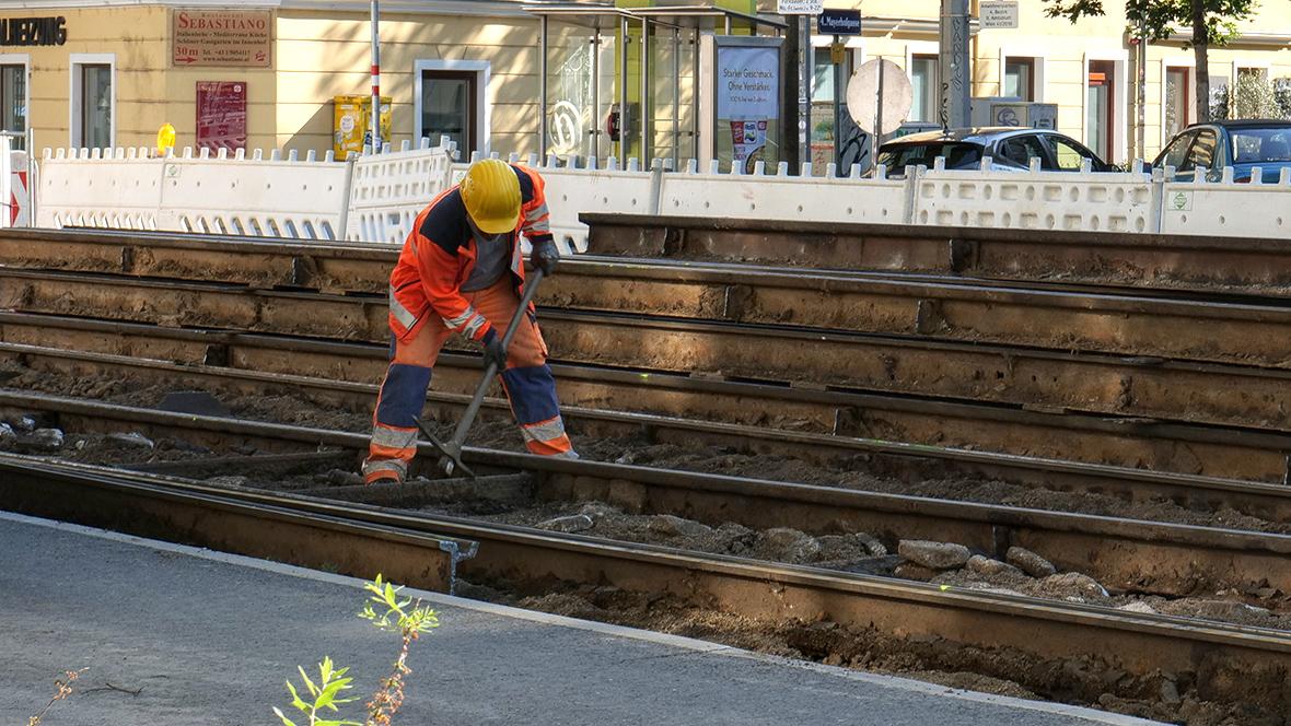 ein Arbeiter auf einer Gleisbaustelle arbeitet mit einem Pickel zwischen den Gleisen
