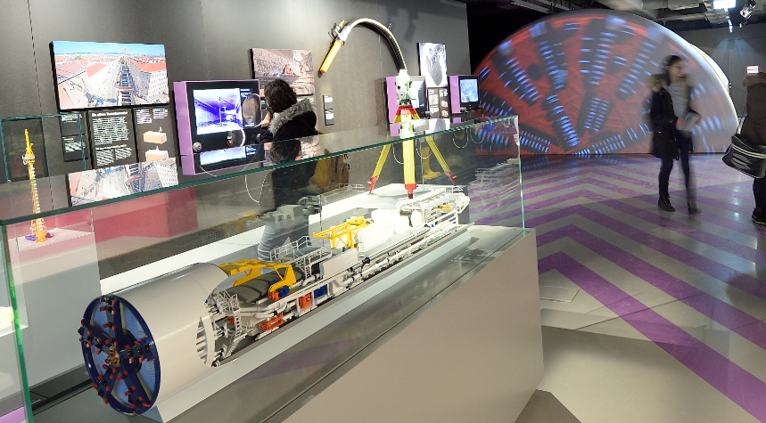 Visitors to the Infocenter look at exhibits in the foreground the model of a tunnel boring machine