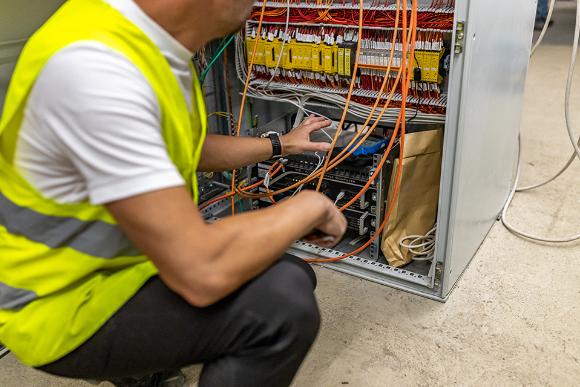 ein Techniker kniet vor einem offenen Schaltkasten mit vielen Kabeln 