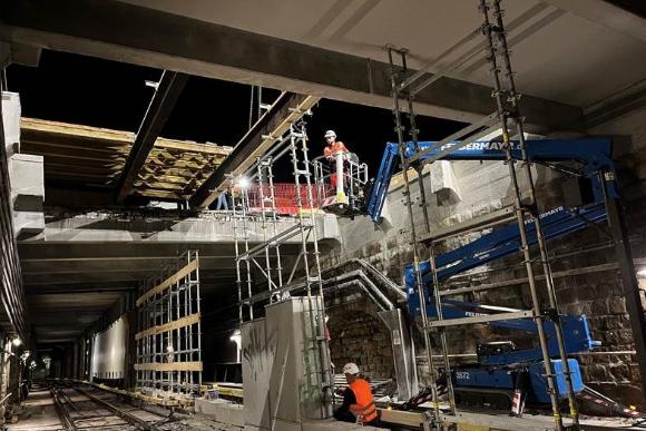 eine Hebebühne hebt einen Arbeiter von unten durch ein Loch in der Tunneldecke