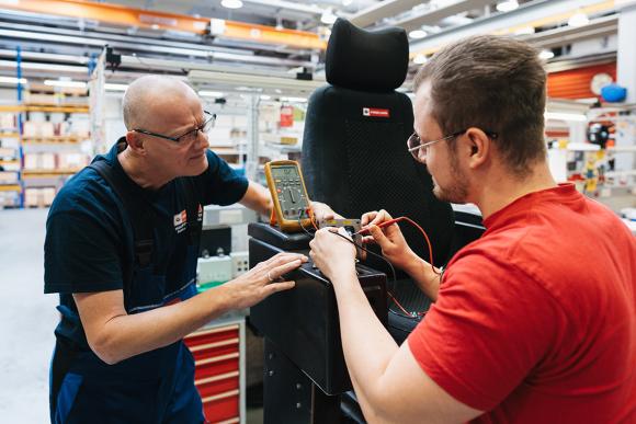 Zwei Männer arbeiten in einer Werkstätte an der Elektronik eines Straßenbahn-Fahrersitzes