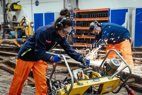 eine junge Frau in Arbeitskleidung und Gehörschutz in einer Werkstätte