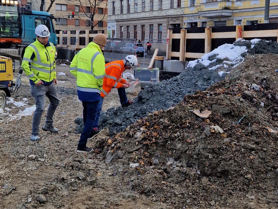 drei Männer in bunten Arbeitsjacken stehen neben einem Erdhaufen einer prüft eine Handvoll Erde