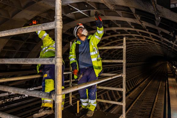 Arbeiter mit Schutzmasken stehe auf einem Gerüst im U1 Tunnel nach dem Brand