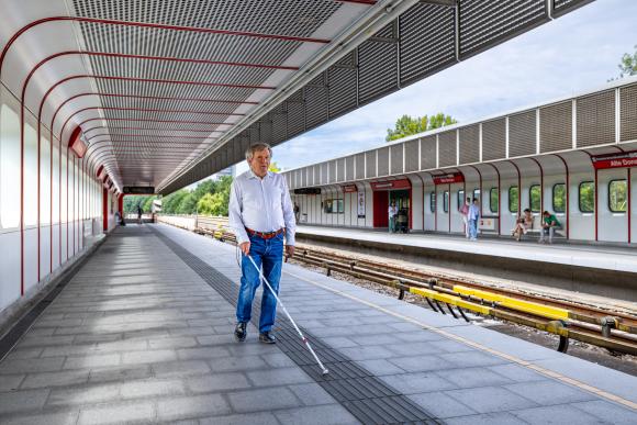 Seheingeschränkte Person orientiert sich mit Blindenstock am taktilen Leitsystem in der U-Bahn-Station