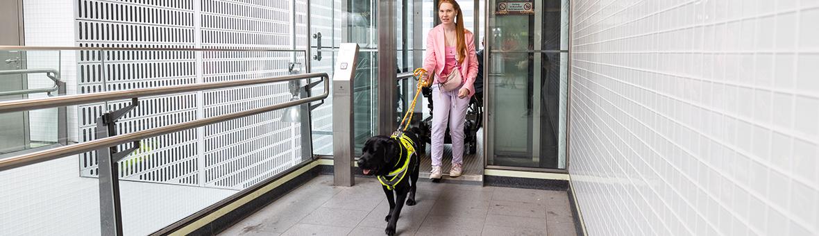 eine Frau mit Assistenzhund verlässt einen Aufzug