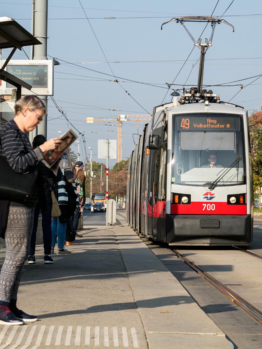 Straßenbahn der Linie 49 fährt in eine Haltestelle ein dort stehen Menschen