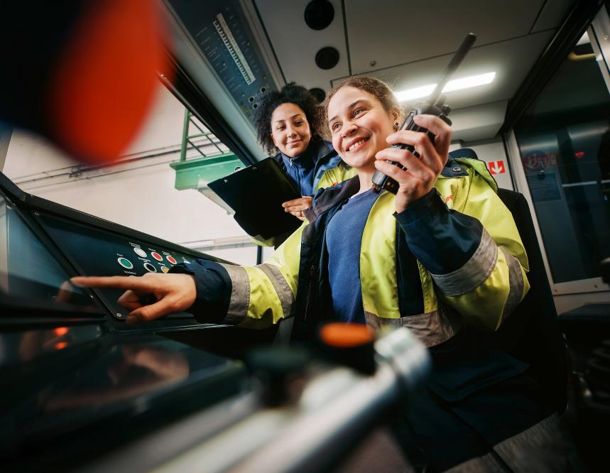 Zwei junge Frauen in der U-Bahn-Fahrerkabine mit Klemmbrett und Telefon in der Hand